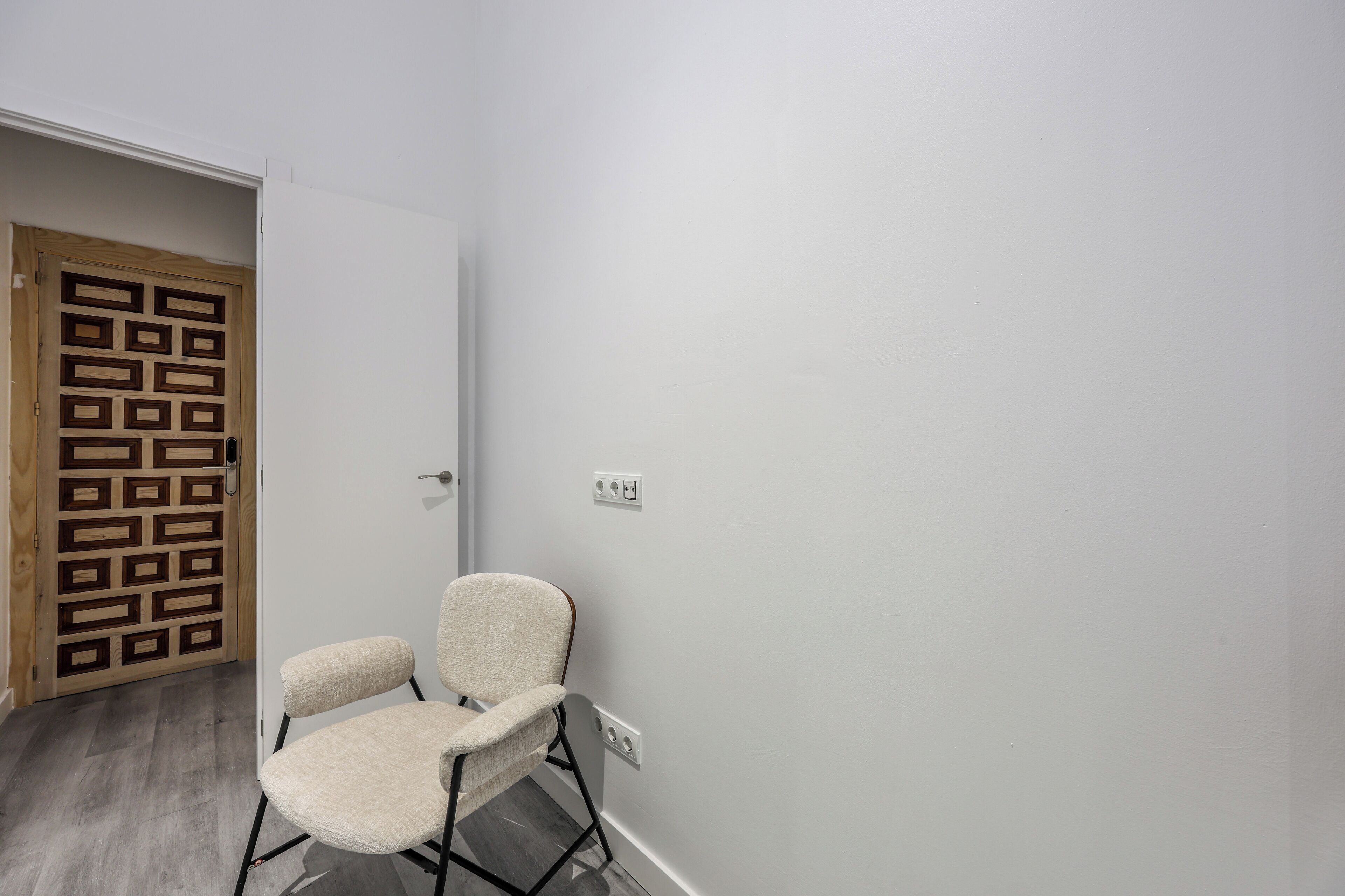 A room with a wooden door, a white wall, and a chair.