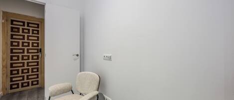 A room with a wooden door, a white wall, and a chair.