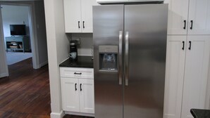 Uma cozinha com armários brancos, geladeira de aço inoxidável, cafeteira e dispenser de água.