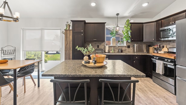 A modern kitchen with dark cabinets, granite countertops, stainless steel appliances, and a large island with bar stools.