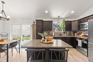 Une cuisine moderne avec des meubles de couleur sombre, des comptoirs en granit, des appareils électroménagers en acier inoxydable et un grand îlot central doté de tabourets de bar.