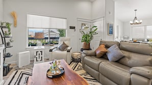 A modern living room with a leather sofa, a wooden coffee table, and a large window with a view of a fenced area.