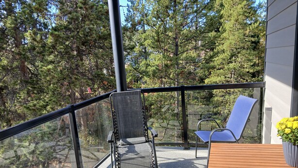 A balcony with a glass railing, two chairs, and a table. - Home away from Home. Recent secure building. Completely equipped kitchen. (Whitehorse)