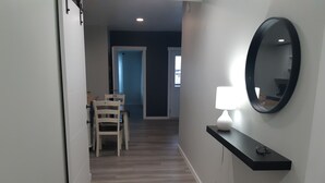 A hallway with a dining area, a black console table with a lamp, and a mirror on the wall. - Home away from Home. Recent secure building. Completely equipped kitchen. (Whitehorse)