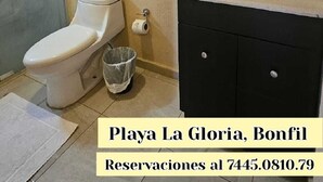 A bathroom with a toilet, sink, and mirror. There is a trash can and a towel on the floor. The text indicates it's in Playa La Gloria, Bonfil, with a reservation number. - Oasis Suite with Ocean View Breakfast Included.  AcapulcoDiamante a (acapulco de juarez)