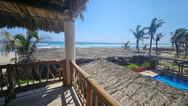 A beach view from a wooden deck with a pool, palm trees, and a thatched roof structure. - Oasis Suite with Ocean View Breakfast Included.  AcapulcoDiamante a (acapulco de juarez)