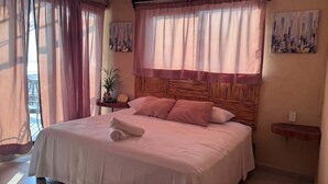 A bedroom with a bed, pillows, a bedside table, a potted plant, and artwork on the walls. - Oasis Suite with Ocean View Breakfast Included.  AcapulcoDiamante a (acapulco de juarez)