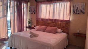A bedroom with a bed, pillows, a bedside table, a potted plant, and artwork on the walls. - Oasis Suite with Ocean View Breakfast Included.  AcapulcoDiamante a (acapulco de juarez)