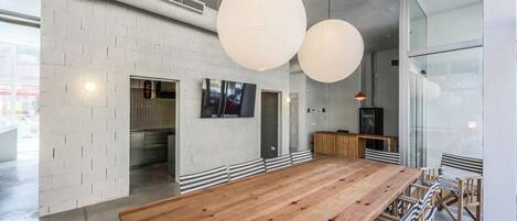 A spacious dining area with a long wooden table and striped chairs, large hanging paper lanterns, and a modern kitchen in the background.