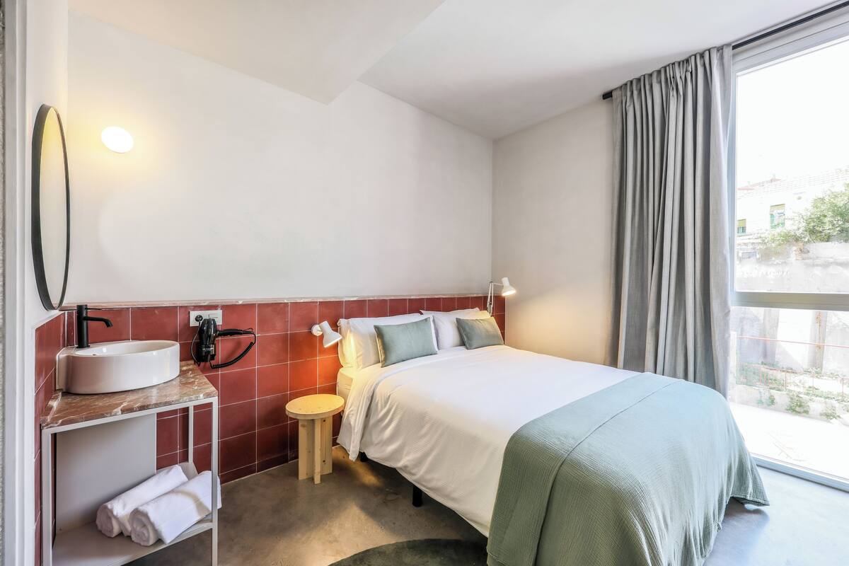 Une chambre d’hôtel avec un lit, une table de chevet avec une lampe, un miroir rond et un lavabo avec une serviette.