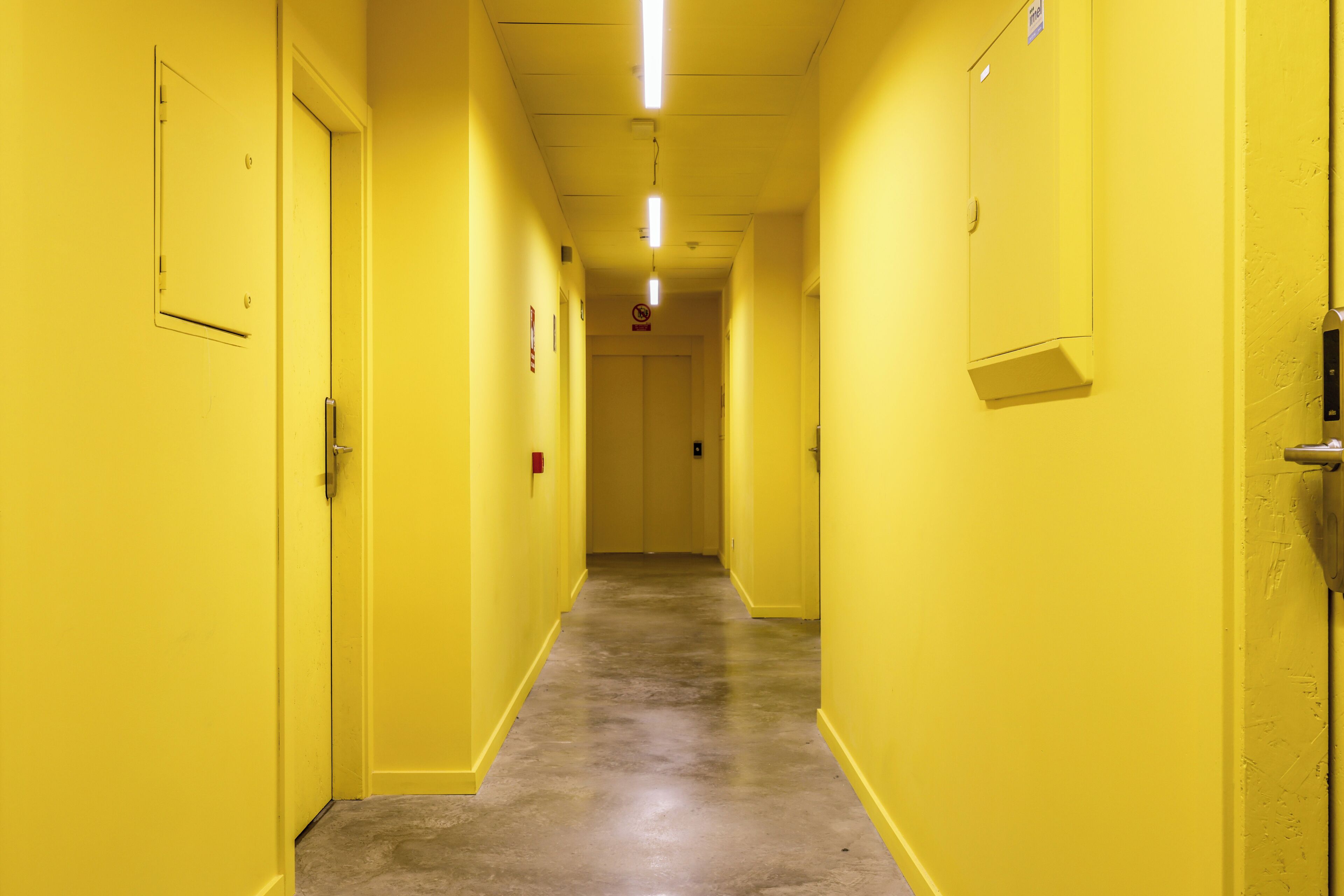 Un long couloir étroit aux murs jaunes et au sol en béton.