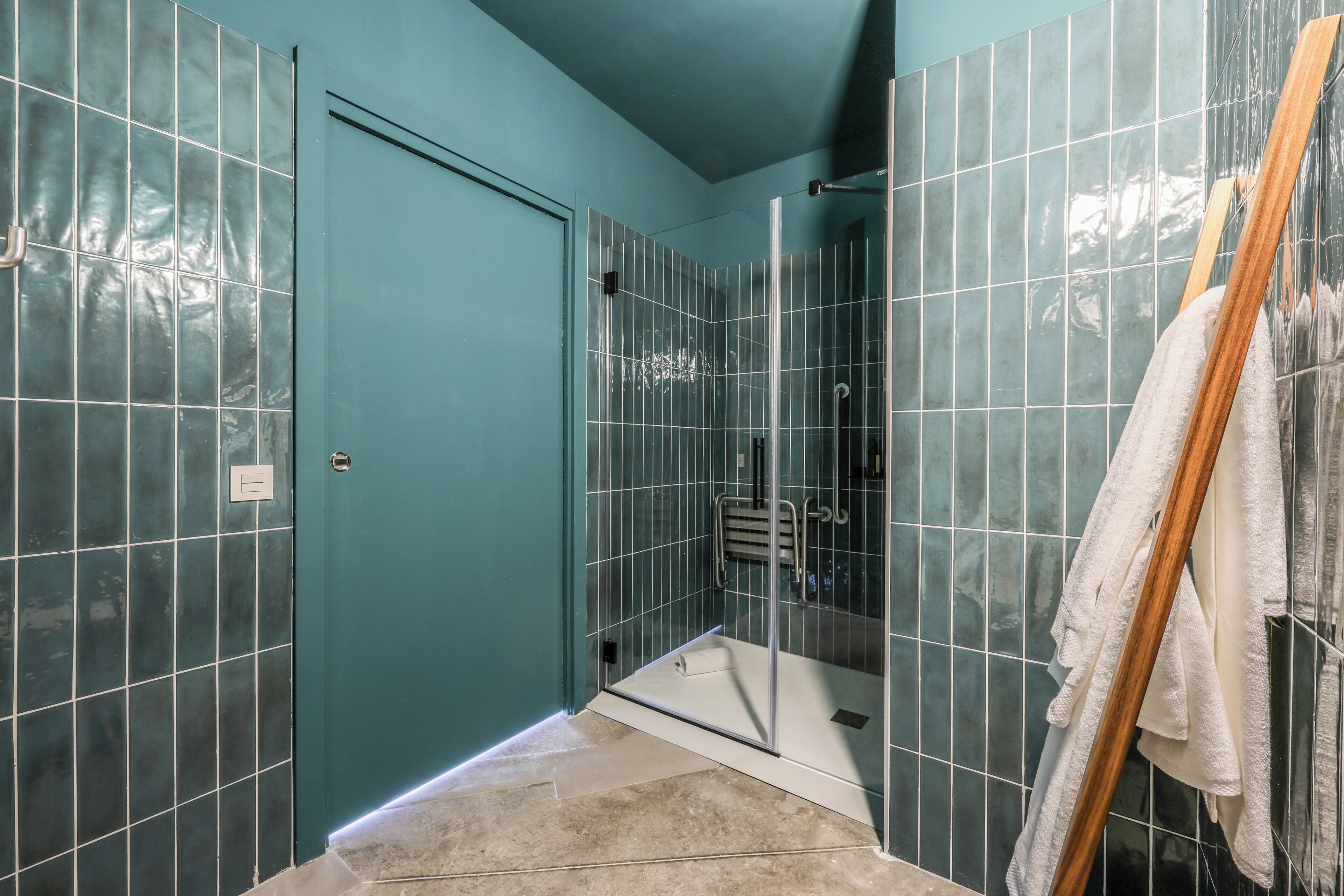 A bathroom with teal walls, a glass shower enclosure, and a wooden towel rack.