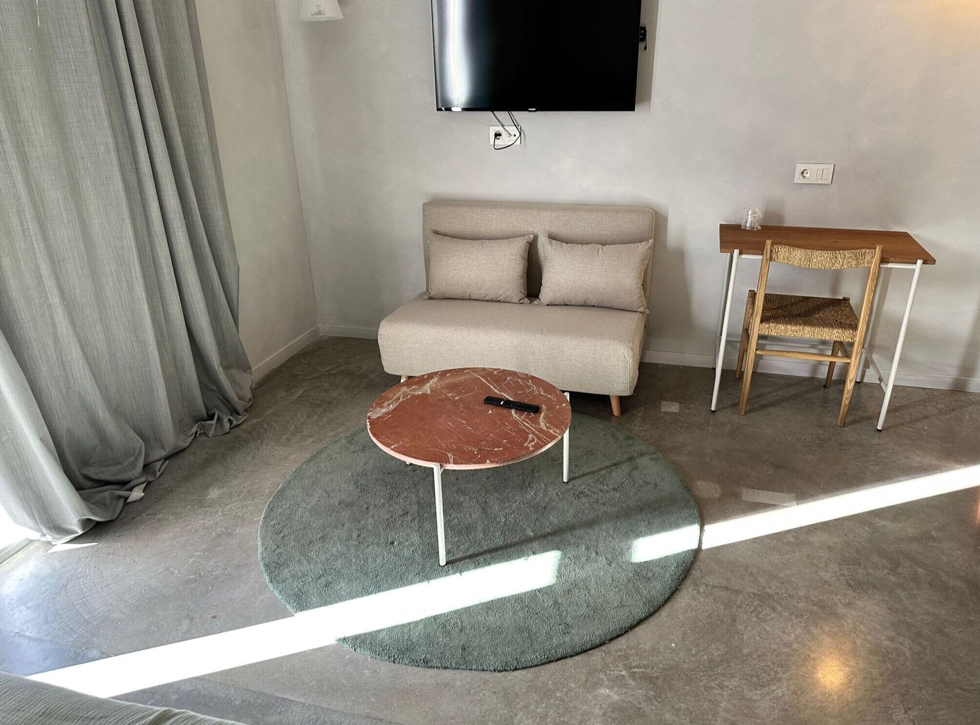 Un salon comprenant un canapé, une table basse, un téléviseur fixé au mur et une petite table en bois avec une chaise.