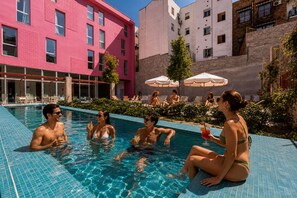 A swimming pool with people relaxing and sunbathing, surrounded by buildings and outdoor seating. - Password to Madrid Casa de Campo (Self Check in) (Madrid)