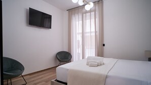 Een moderne hotelkamer met een groot bed, een flatscreen televisie aan de muur, een stoel en een raam met dunne gordijnen.