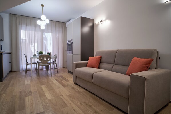 A modern living room with a sofa, a dining table with chairs, and a kitchen area with an oven. - Antifemo Cairoli Apartments - Elegance and comfort in the heart of Gela (Gela)