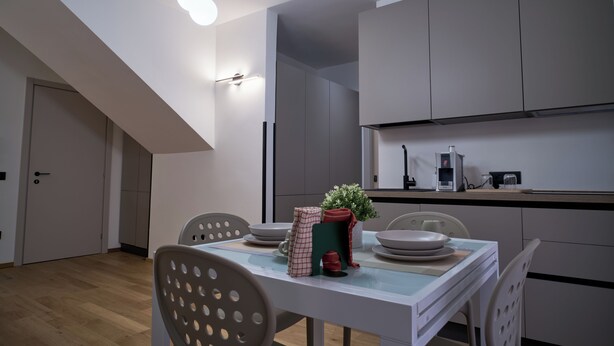 Een moderne keuken met witte kasten, een eettafel met stoelen en een plafondlamp.
