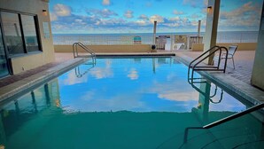 Una piscina interior con agua cristalina y azul, rodeada de paredes de azulejos y un balcón con vistas a la playa.