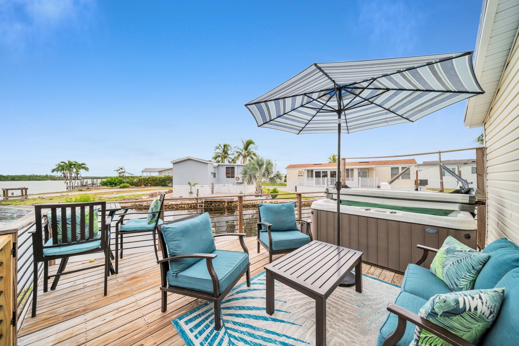 Eine Terrasse mit Gartenmöbeln, einem Whirlpool und Blick auf einen See und Häuser.