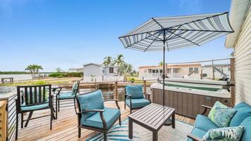 Eine Terrasse mit Gartenmöbeln, einem Whirlpool und Blick auf einen See und Häuser.