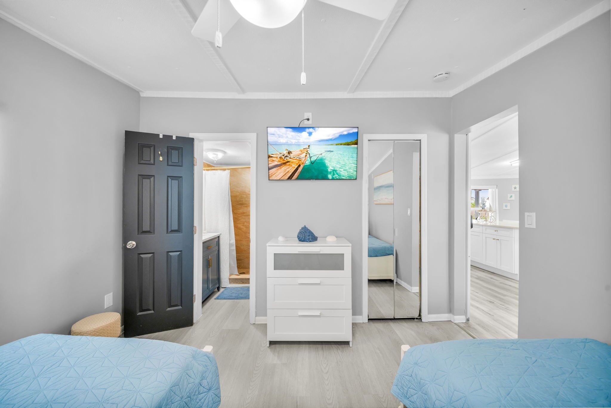 A bedroom with two beds, a TV mounted on the wall, and a door leading to a bathroom.