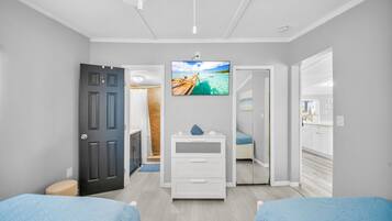 A bedroom with two beds, a TV mounted on the wall, and a door leading to a bathroom.