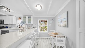 Eine moderne Küche mit weißen Schränken, einer zentralen Kochinsel mit Barhocker und einem Essbereich mit rundem Tisch und Stühlen.