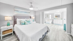 Ein Schlafzimmer mit einem großen Bett, Nachttischlampen, einem Deckenventilator und Blick ins Badezimmer.