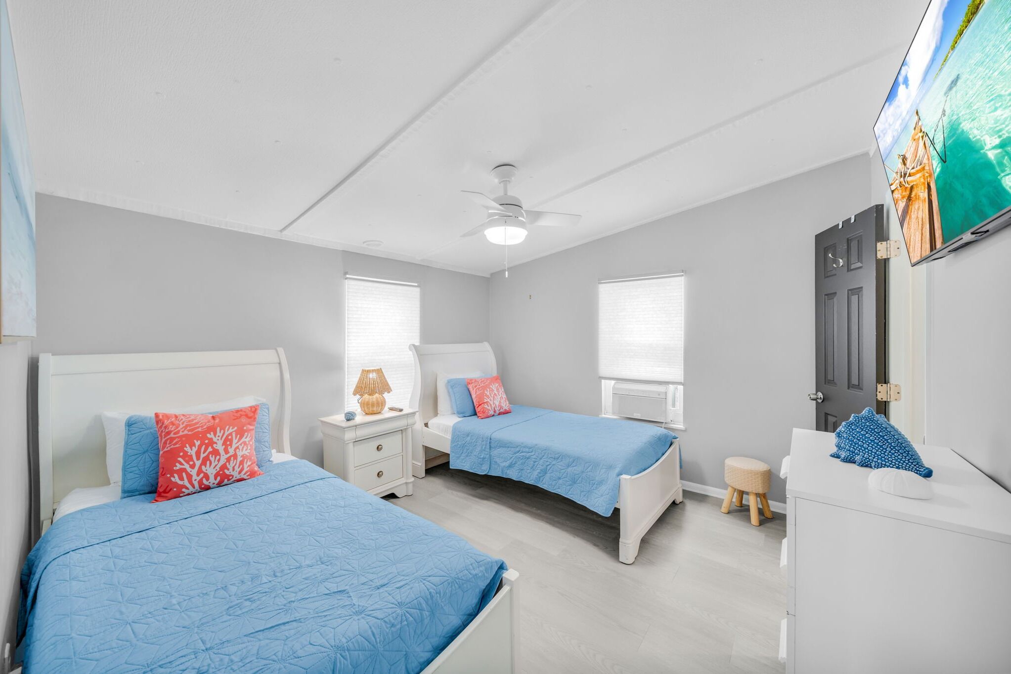 A bedroom with two beds, a ceiling fan, and a TV on the wall.