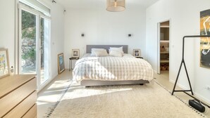 A bedroom with a large bed, a standing lamp, and a view of a garden through the window.