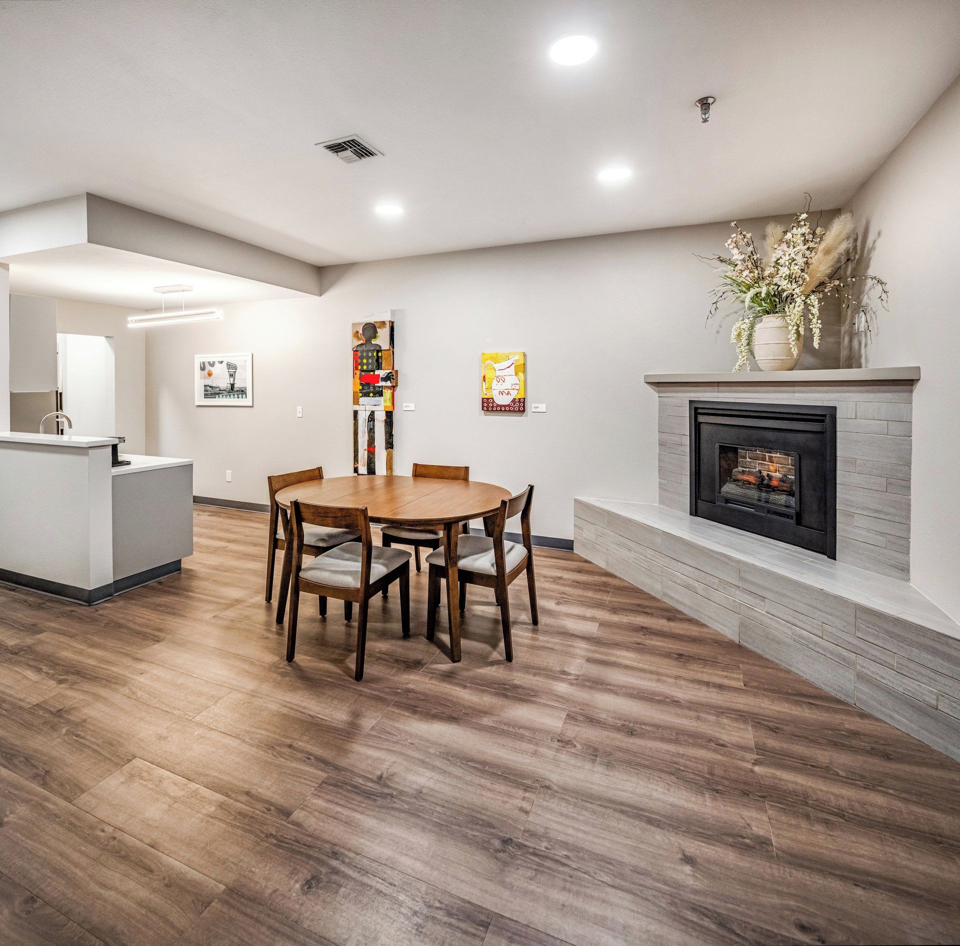 A modern dining area with a wooden table and chairs, a fireplace, and artwork on the walls.