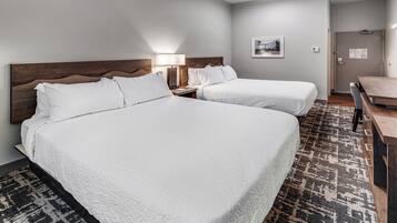 Quarto de hotel com duas camas, uma escrivaninha, uma cadeira, um abajur e um quadro na parede.