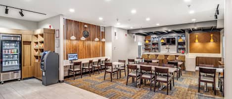 Vestíbulo de hotel con zona de estar, máquina de bebidas, bar y un muro decorativo de madera.
