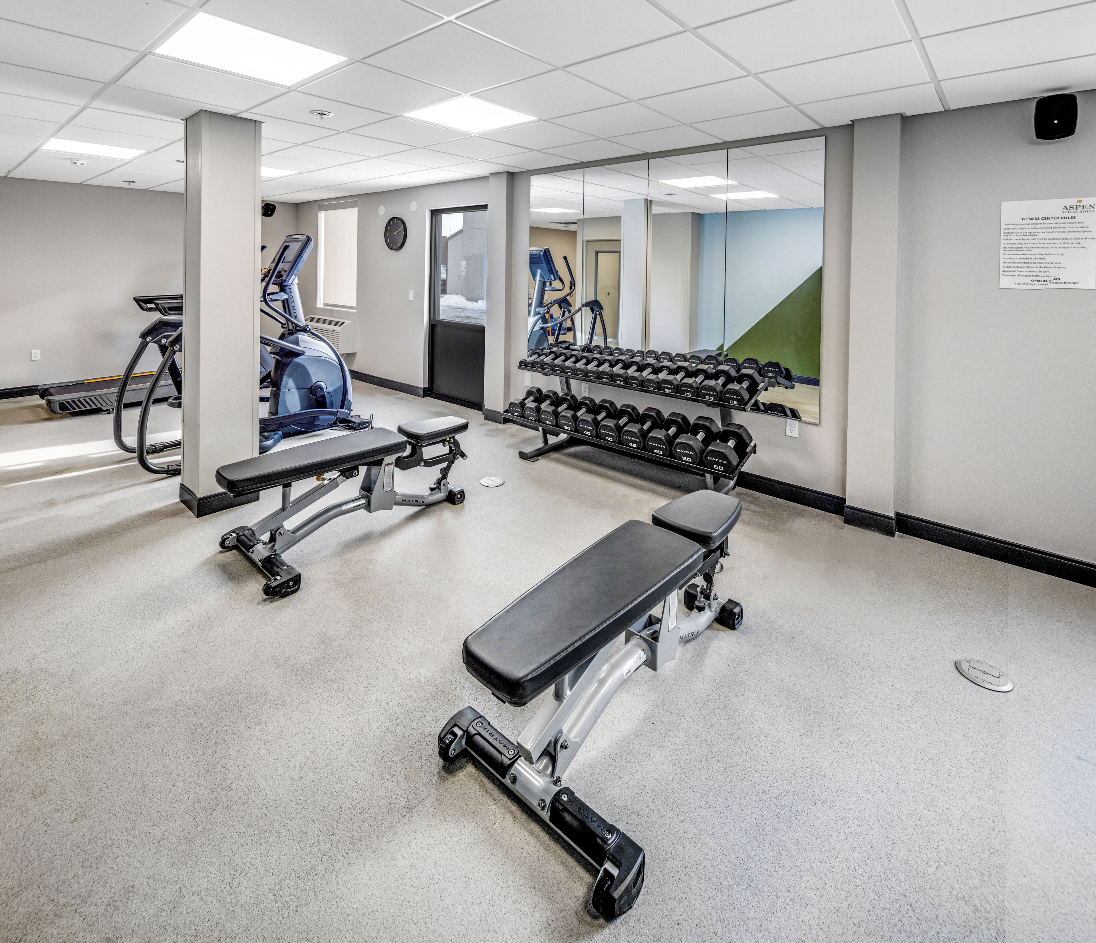 Een sportschool met trainingsapparatuur, banken en gewichten.