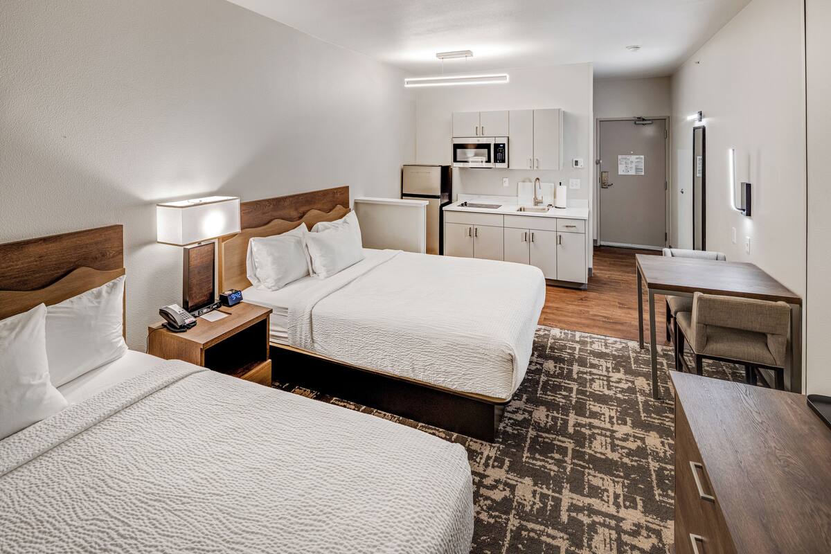 Ein Hotelzimmer mit zwei Betten, einem Schreibtisch, einer Küchenzeile und einem Badezimmer.