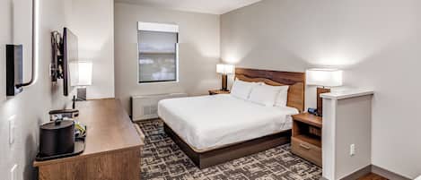 Una habitación de hotel moderna con una cama, mesitas de noche, un escritorio, un espejo, una ventana y una lámpara en el techo.