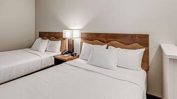 A hotel room with two beds, a nightstand with a lamp, a phone, and a clock.