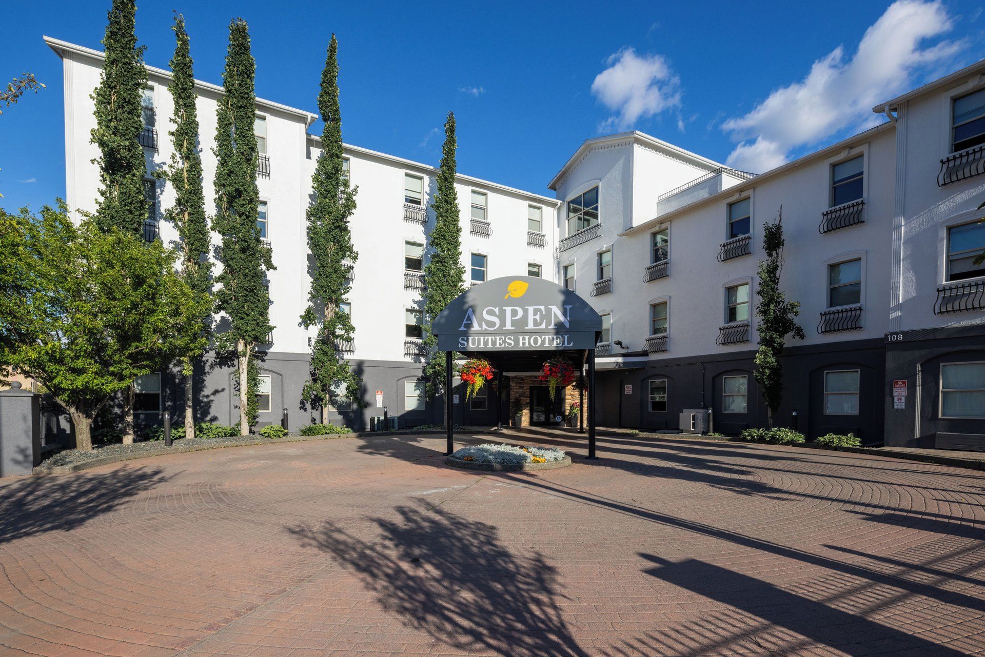 L’entrée d’un hôtel, avec une enseigne indiquant « Aspen Suites Hotel », entourée d’immeubles et d’arbres.