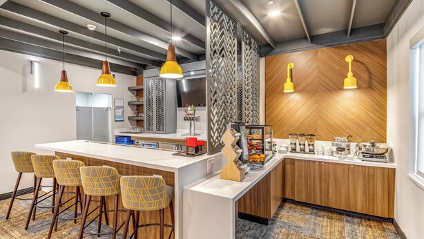 A modern kitchen with a bar area, wooden accents, and a patterned carpet. - Aspen Suites Hotel Anchorage Downtown (Anchorage)