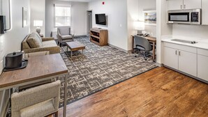 A modern living room with a sofa, coffee table, and TV. There's a kitchen area with a microwave and cabinets. - Aspen Suites Hotel Anchorage Downtown (Anchorage)
