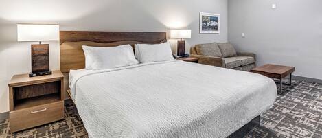 Una camera d'albergo con un letto grande, due comodini con lampade, una testiera in legno, un divano piccolo e un tappeto a motivi.