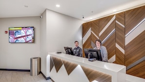 A reception desk with a modern design, a mounted television, and a trash can. - Aspen Suites Hotel Anchorage Downtown (Anchorage)