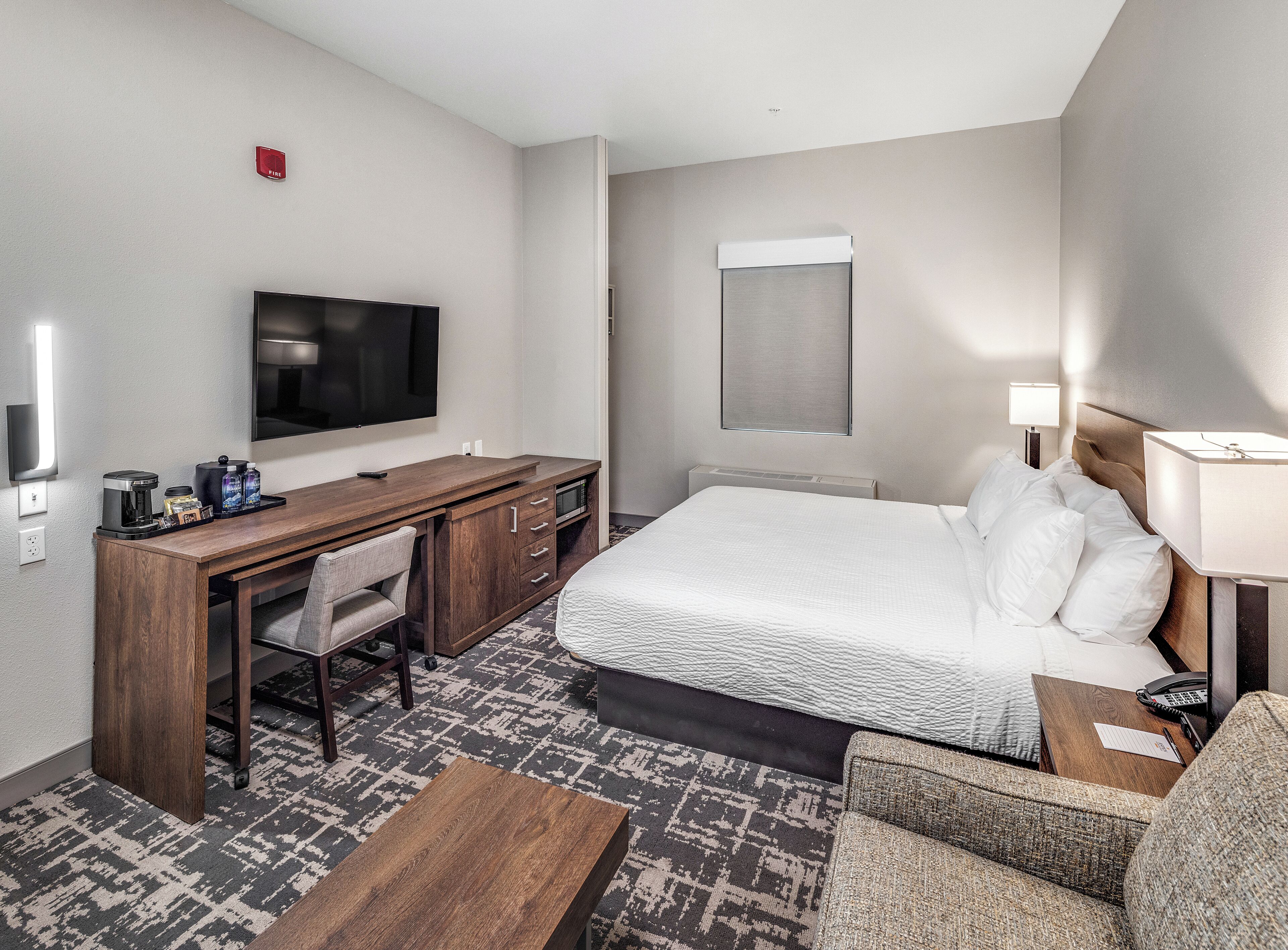 A hotel room with a bed, a desk with a TV, a coffee maker, and a lamp.