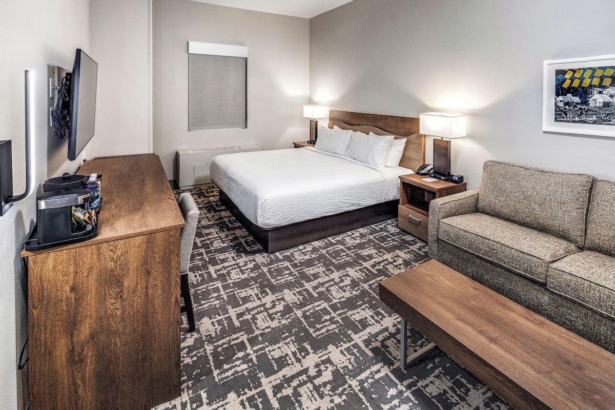 Ein Hotelzimmer mit Bett, Nachttischen, Fernseher, Kaffeemaschine, einer Couch und einem gemusterten Teppich.