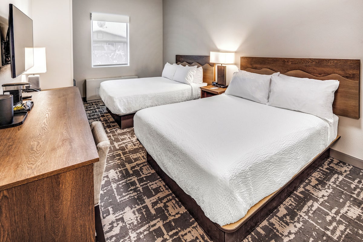 Ein Hotelzimmer mit zwei Betten, einem Schreibtisch, einem Fernseher und einem Fenster.
