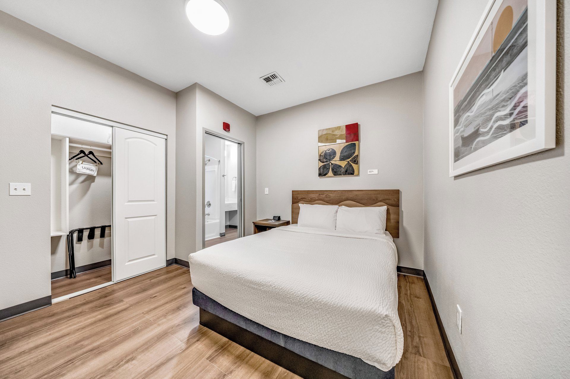 A hotel room with a bed, a wardrobe, a bathroom, and a painting on the wall.