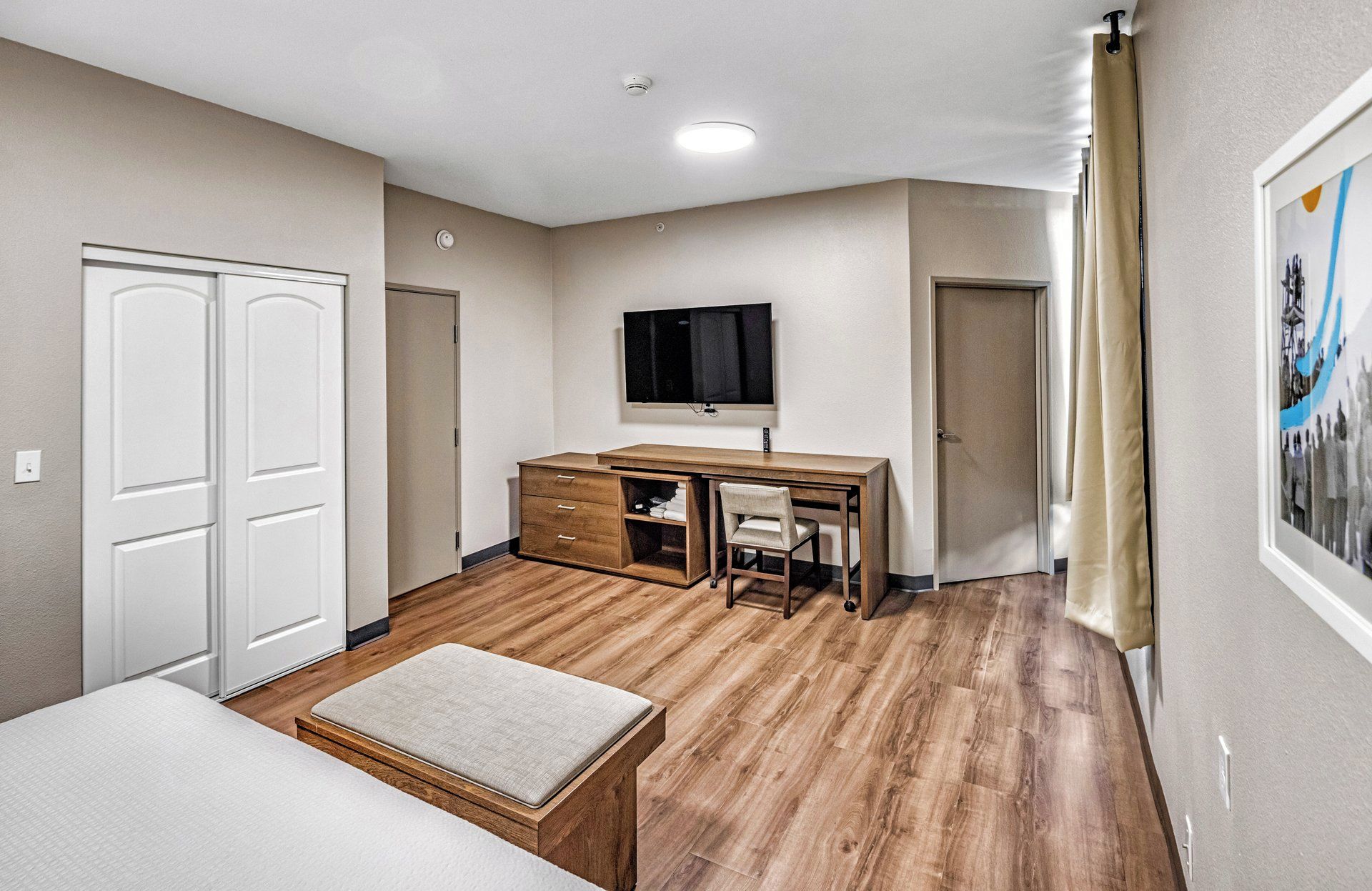 Un dormitorio con cama, escritorio, silla, televisor y puerta.