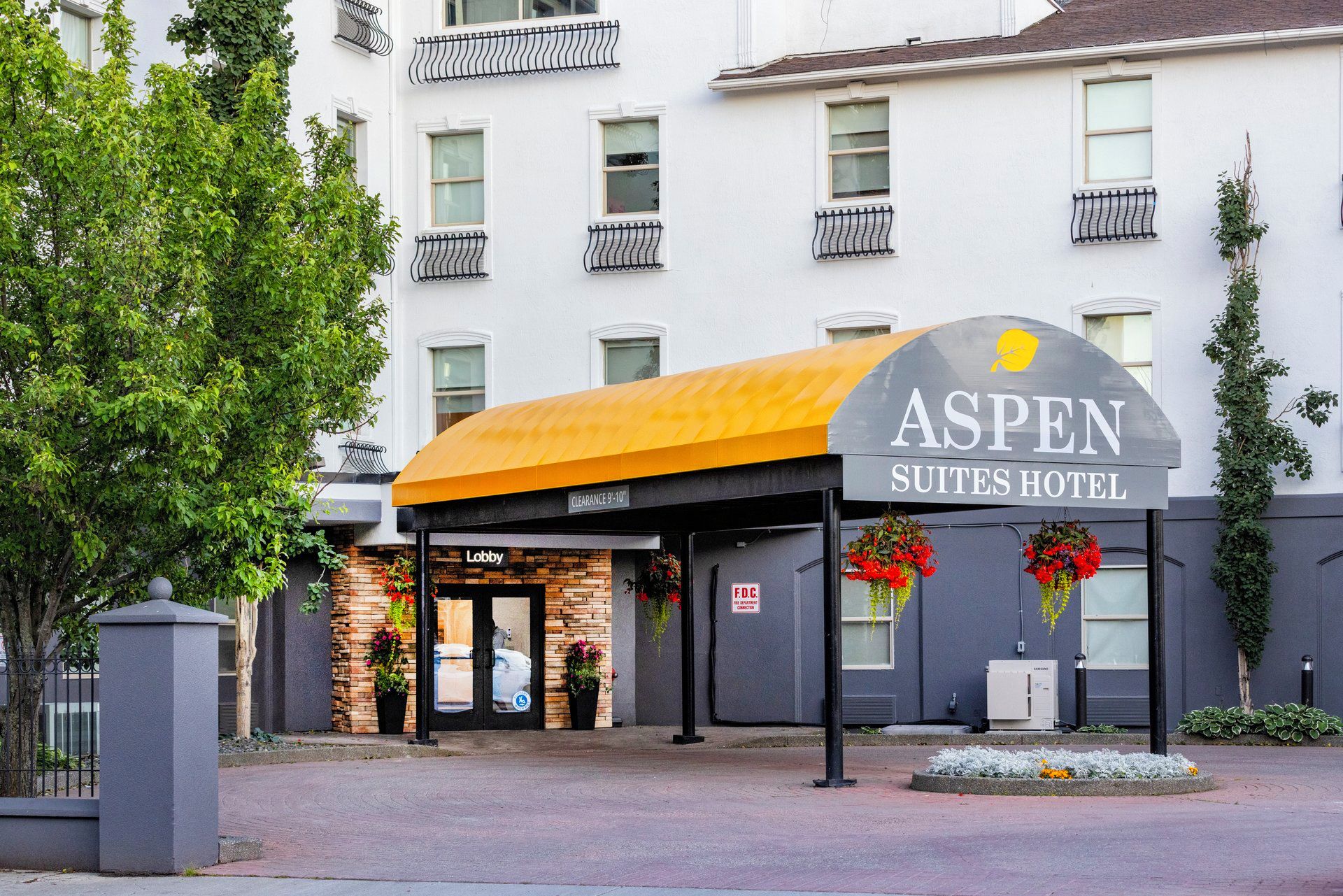 The Aspen Suites Hotel entrance with a clear sign, a lobby entrance, and a covered waiting area.