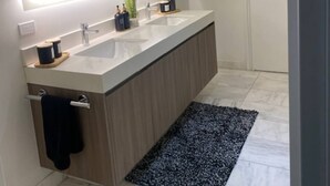 A modern bathroom with a large mirror, two sinks, a towel rack, and a potted plant.