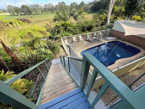 A swimming pool with a wooden deck and a fence, surrounded by lush greenery.